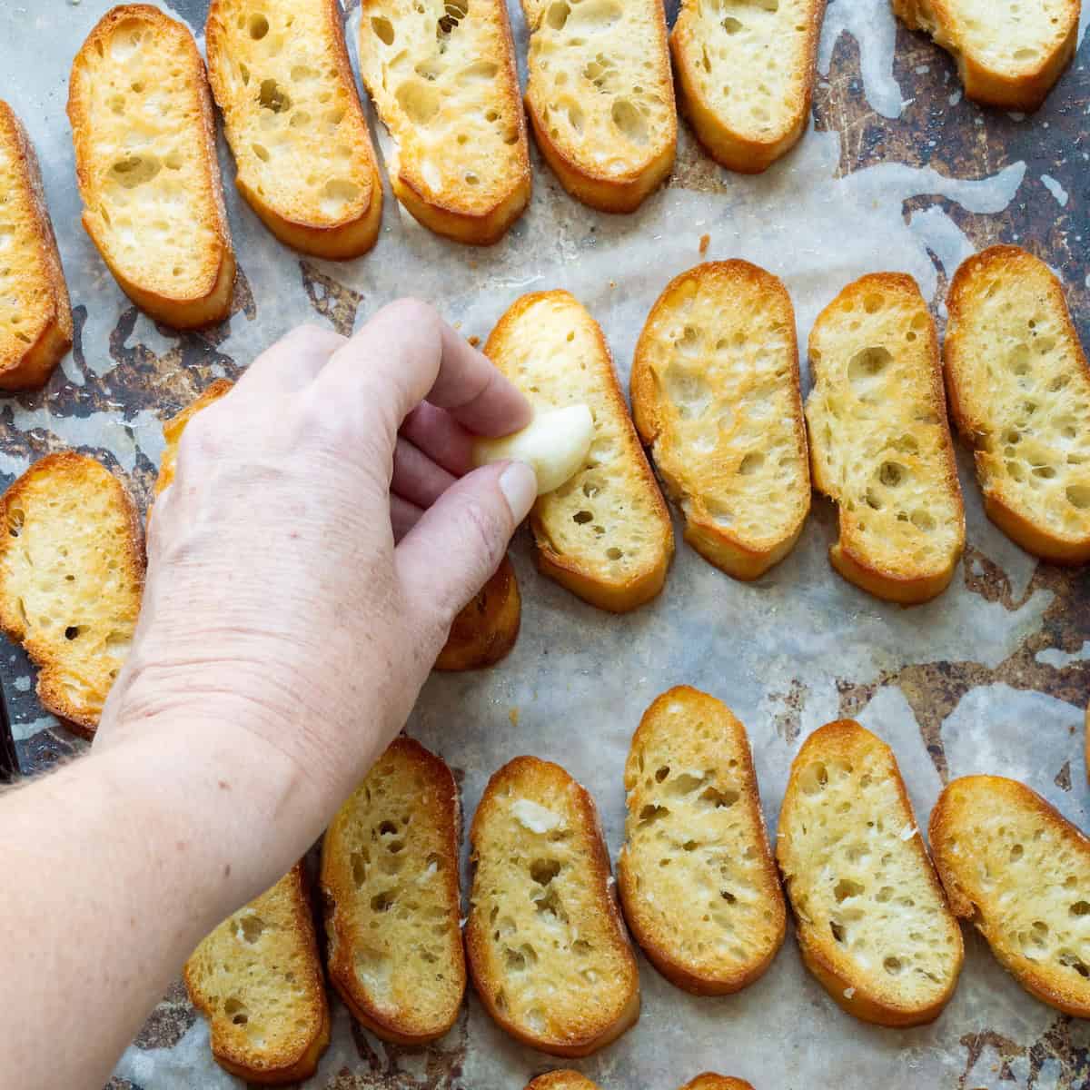 Rubbing cut cloves of garlic onto small toasted baguette slices.