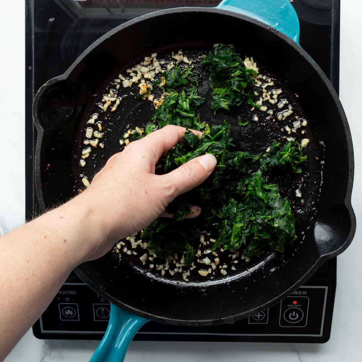 Adding thawed frozen spinach to a skillet with sautéed garlic.