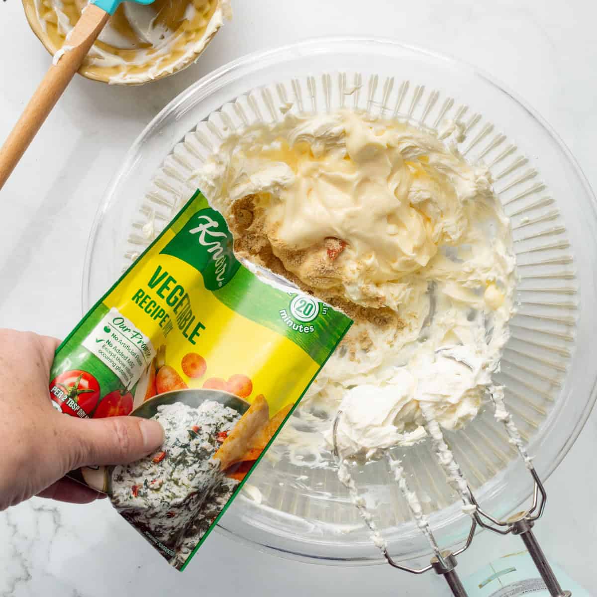 Adding Knorr vegetable dip mix to a bowl of mayonnaise and cream cheese.