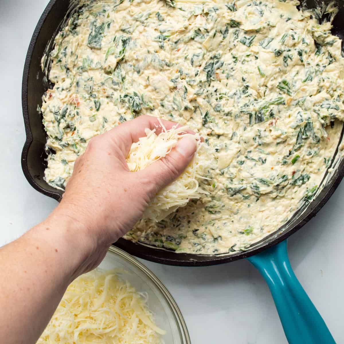 Sprinkling the top of spinach artichoke dip filling with mozzarella and Parmesan cheeses.