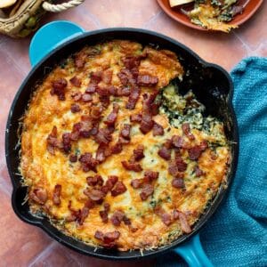Hot Knorr spinach artichoke dip with bacon in a blue handled cast iron skillet.