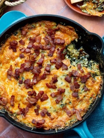 Hot Knorr spinach artichoke dip with bacon in a blue handled cast iron skillet.