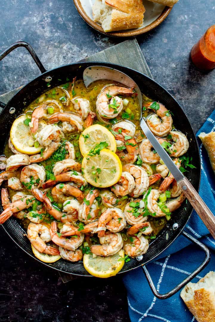 New Orleans BBQ shrimp recipe with plump shrimp in a buttery, seasoned sauce, topped with lemon slices, green onions, and fresh parsley.