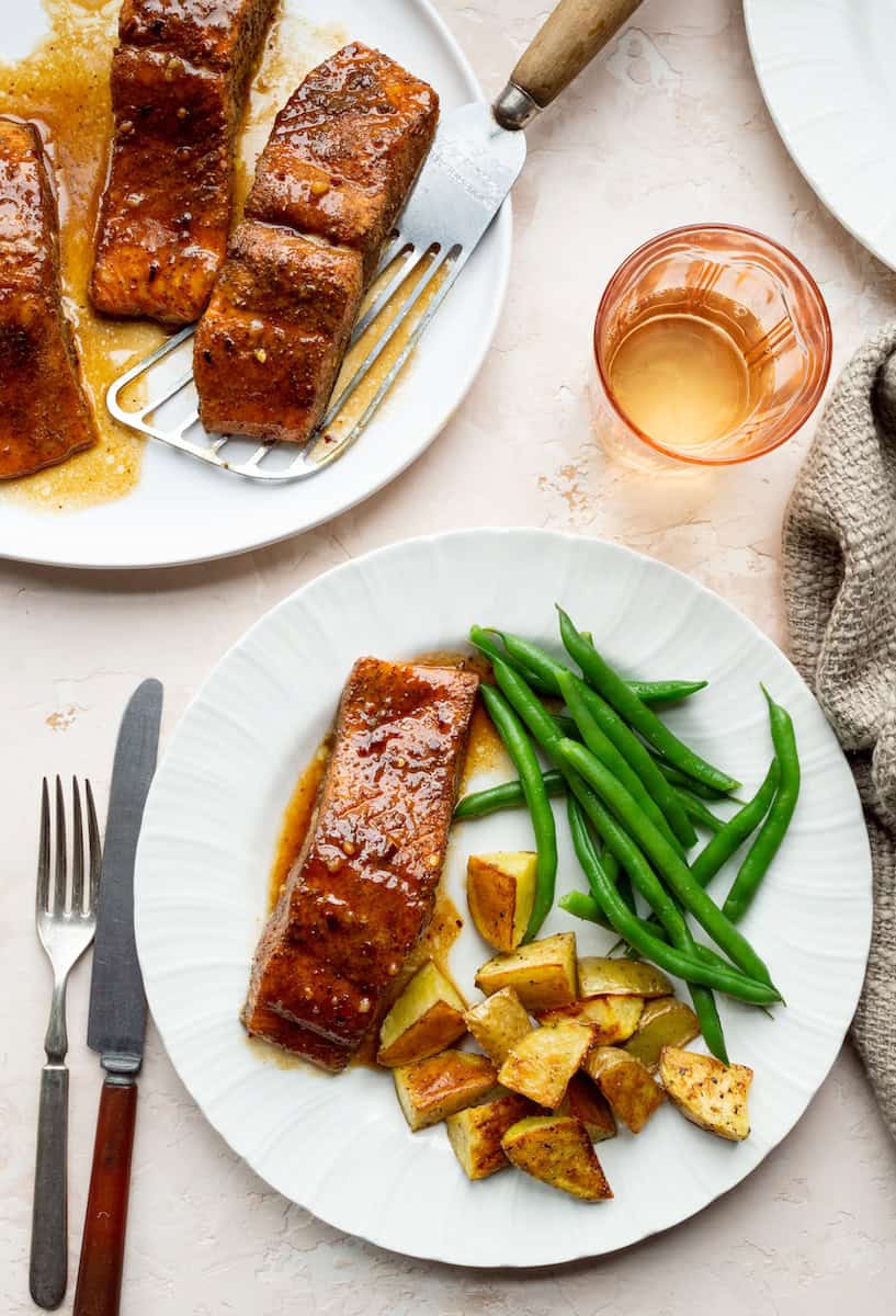 Old Bay salmon recipe with honey butter glaze, served on a white plate with roasted potatoes and green beans.