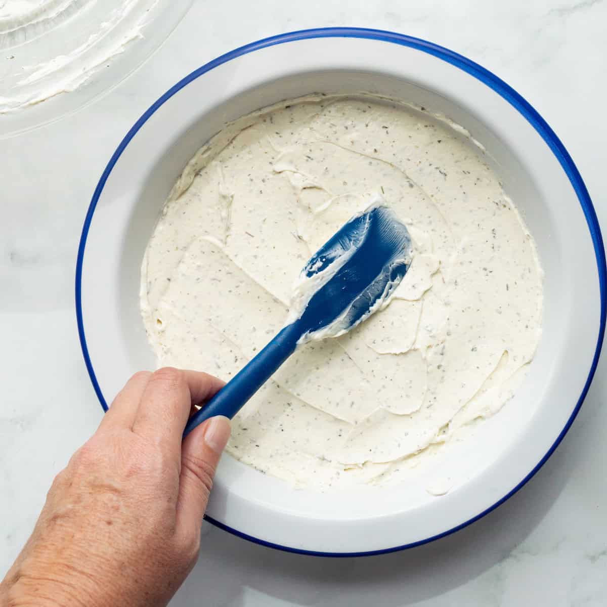 Spreading Italian seasoned cream cheese in the bottom of a round baking dish.
