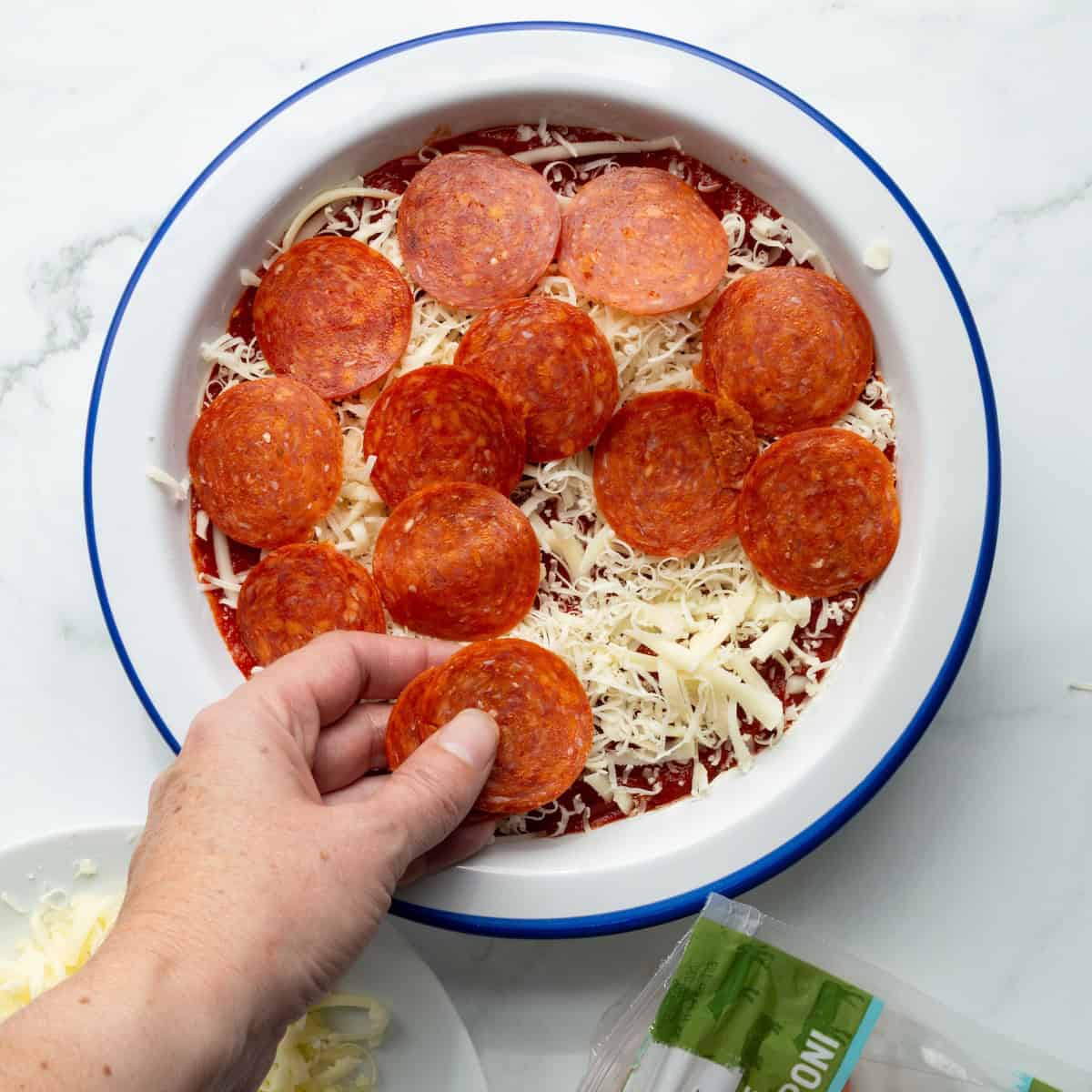 Layering mozzarella cheese and pepperoni slices in a casserole dish for pepperoni pizza dip.