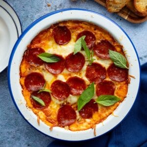 A blue rimmed round white casserole dish filled with pepperoni pizza dip.