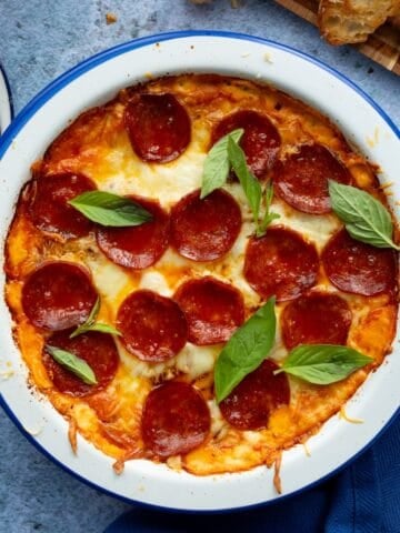 A blue rimmed round white casserole dish filled with pepperoni pizza dip.