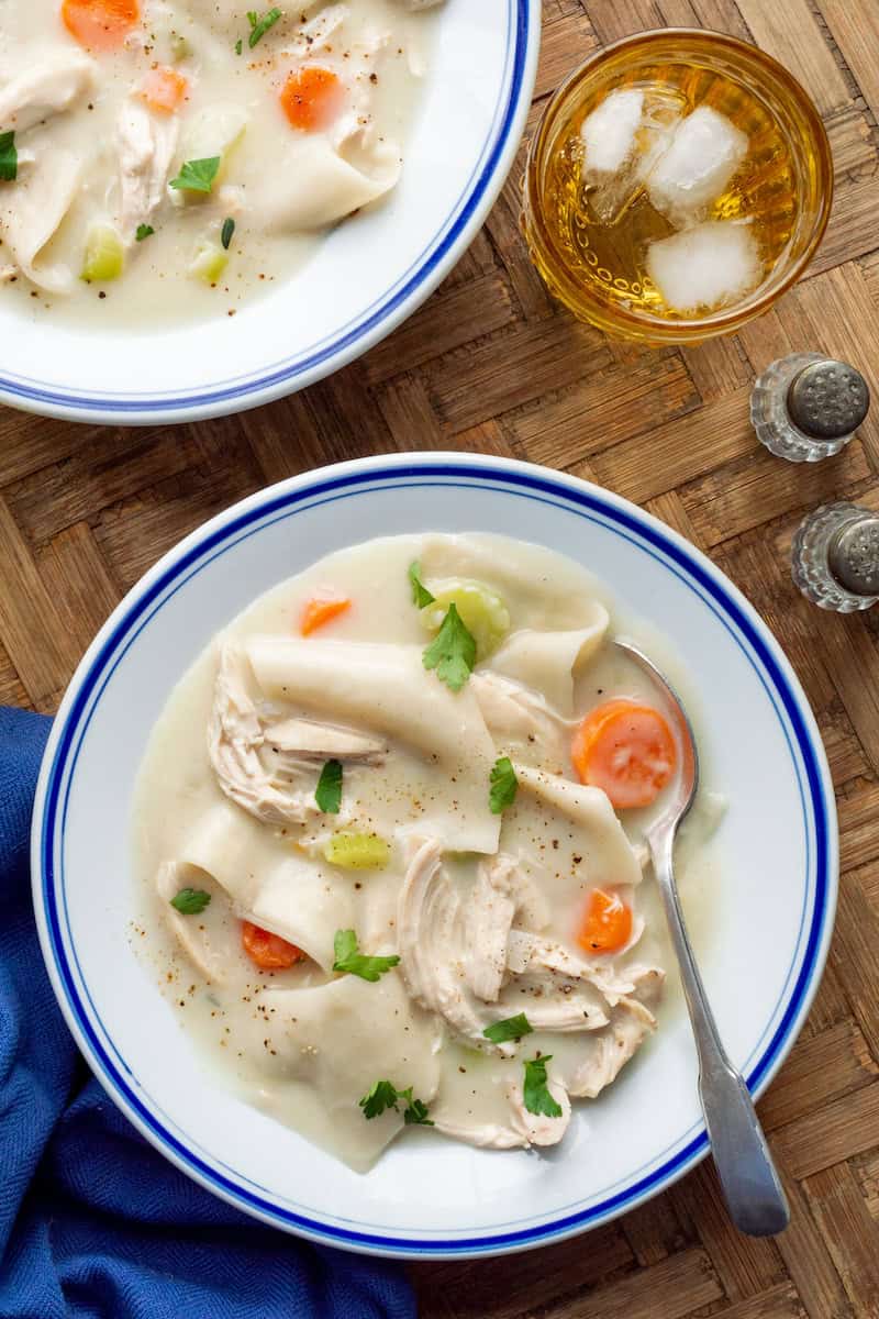 Shortcut Anne's chicken and dumplings with shredded chicken, flat dumplings, carrots, and celery in a creamy broth, garnished with parsley.