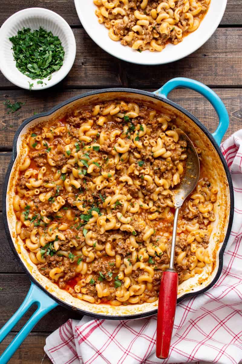 Hamburger helper without milk made with elbow macaroni, seasoned ground beef, and creamy tomato sauce, topped with fresh parsley in a skillet.