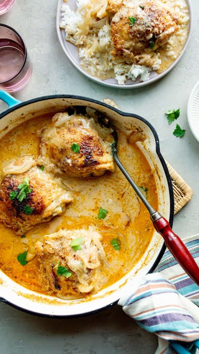 Smothered chicken thighs cooked in creamy onion gravy and topped with fresh parsley, served in a skillet with a side of white rice.