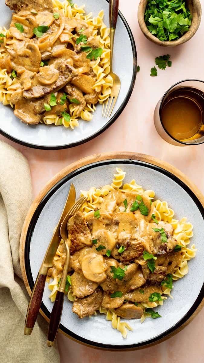 Stroganoff noodles with steak, sliced mushrooms, and creamy gravy served over buttered egg noodles, topped with fresh parsley.